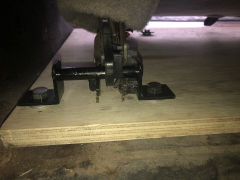 1980 Ford Bronco - A close-up view shows the underside of a seat mechanism bolted to a wooden platform. Metal brackets and bolts are visible, securing the mec…