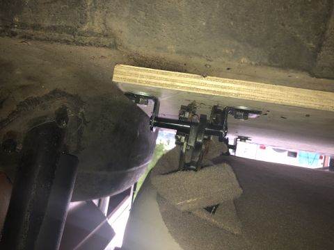 1980 Ford Bronco - A close-up view of the underside of a vehicle, showing a wooden support attached with metal brackets and bolts to a large, dark-colored tan…