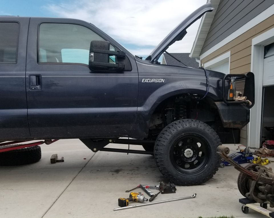 Dark blue Ford Excursion with hood open, showing suspension work in a driveway.