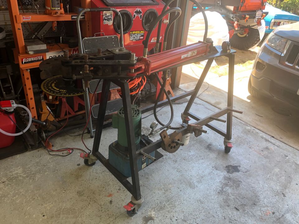 Red hydraulic tube bender on a black metal stand in a garage.