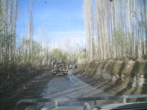 1981 Ford Bronco - Military vehicles traverse a muddy path through a wooded area.