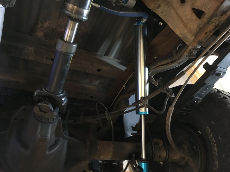 Underneath a vehicle showing a new aluminum remote-reservoir shock installed at the rear axle near the driveshaft