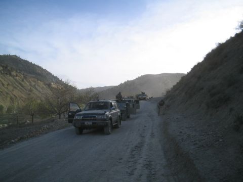 1981 Ford Bronco - A convoy of Toyota Land Cruisers drives down a dusty mountain road under a hazy sky.