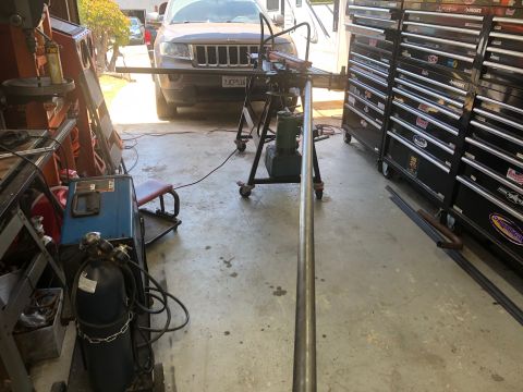 1992 Jeep Wrangler - A metal pipe is being bent on a pipe bender in a garage. In the background, a Jeep Grand Cherokee is parked near the garage opening.