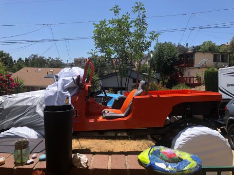 1992 Jeep Wrangler - The orange body of a Jeep Wrangler is parked outdoors, partially covered by a tarp. The vehicle is missing its hood and windshield frame, a…