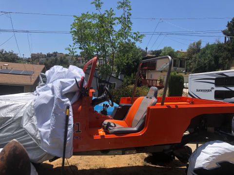 1992 Jeep Wrangler - An orange Jeep Wrangler is partially covered by a white tarp, with its driver's seat and steering wheel visible. A white recreational vehic…