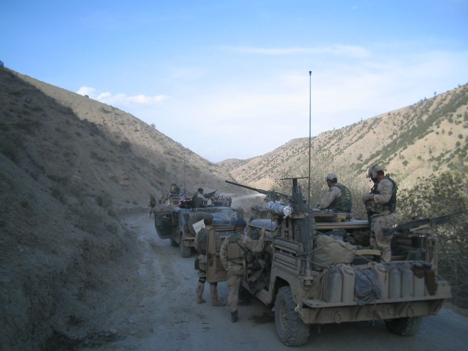 Military convoy on a dirt road with soldiers and vehicles
