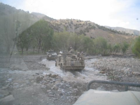 1981 Ford Bronco - Several military vehicles navigate a shallow, rocky stream in a mountainous, arid region.