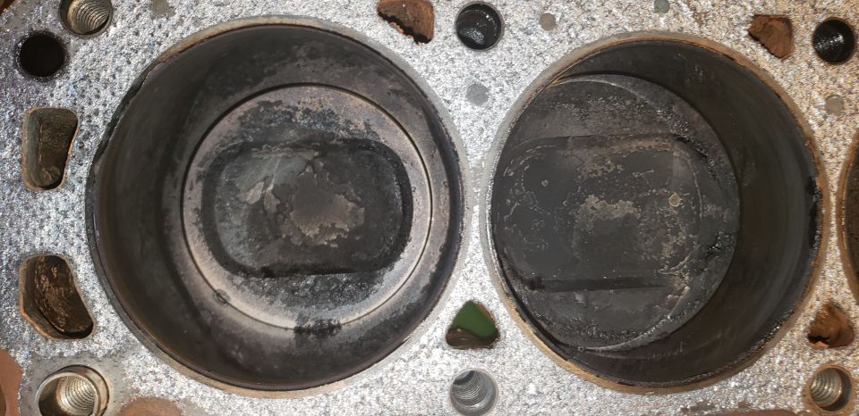 Two engine cylinder bores with carbon-covered pistons visible in a bare engine block deck