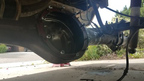 1985 Ford Bronco - The underside of a vehicle's rear axle assembly is shown, with the differential cover removed and a new gasket being installed with several…