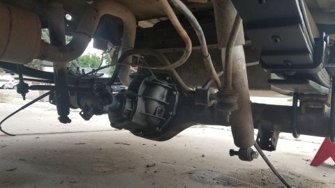 1985 Ford Bronco - The underside of a vehicle's rear axle assembly is shown, featuring the differential, leaf springs, shocks, and exhaust system. The vehicle…