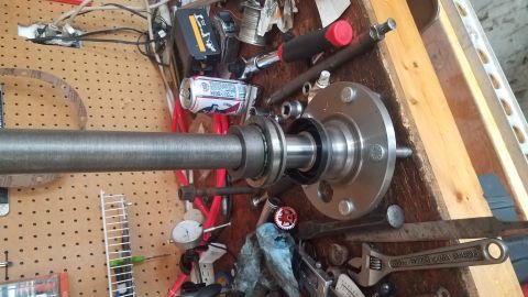 1985 Ford Bronco - A close-up view of a vehicle's axle and hub assembly, with various tools and a can of beer scattered on a wooden workbench.