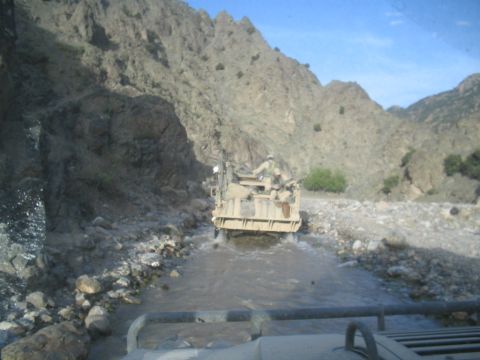 1981 Ford Bronco - A military vehicle navigates a rocky stream bed in a mountainous region.
