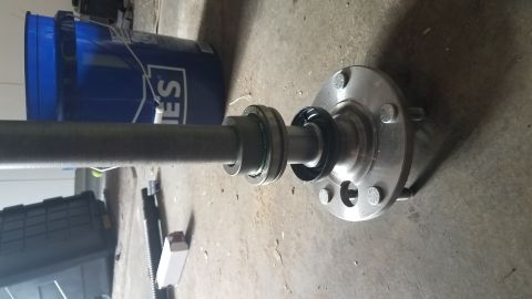 1985 Ford Bronco - A vehicle axle with a hub assembly and bearing is laid out on a concrete floor next to a blue bucket and a black storage container.