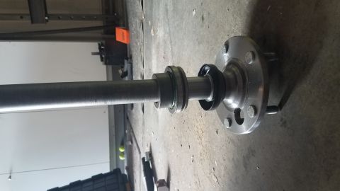 1985 Ford Bronco - A close-up view of a vehicle's axle shaft with a bearing assembly and a flange attached. The axle and components are resting on a concrete…