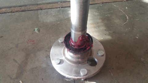 1985 Ford Bronco - A close-up view shows a metal shaft being greased with red lithium grease, inserted into a silver hub assembly with four bolts. The assembl…
