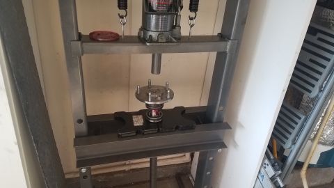 1985 Ford Bronco - A hydraulic press is being used to press a wheel bearing onto a wheel hub assembly. The assembly is positioned on the press's lower support.