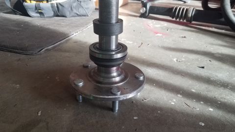 1985 Ford Bronco - A close-up view of a vehicle's wheel hub and bearing assembly resting on a concrete floor. The assembly features a metal flange with severa…