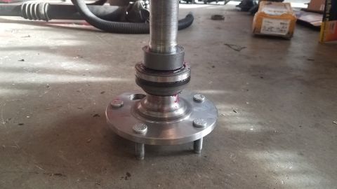 1985 Ford Bronco - A close-up view of a vehicle's wheel hub assembly with a CV joint and bearing, covered in red grease, is mounted on a metal shaft with lug…