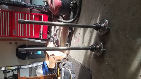 1985 Ford Bronco - Two driveshafts with flanges are laid out on a garage floor in front of a red toolbox and a black shop vacuum.