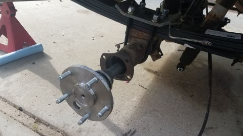1985 Ford Bronco - A close-up view of a rear axle assembly with a new hub and wheel studs installed. The vehicle appears to be on jack stands with the leaf sp…