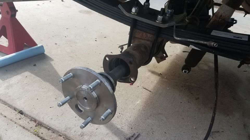 Rear axle assembly with new hub and wheel studs installed, vehicle on jack stands.