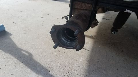 1985 Ford Bronco - Close-up view of a rusty differential housing with four wheel studs attached to a flange. The housing is mounted to leaf springs, and a sho…