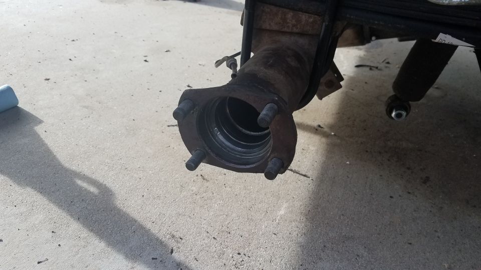 Rusty differential housing with wheel studs attached to a flange, mounted to leaf springs.