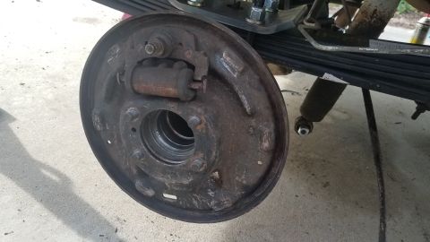 1985 Ford Bronco - A close-up view of a rusty brake drum assembly, likely from a vintage truck or SUV, is shown. The assembly includes the brake drum, wheel c…