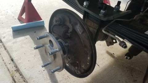 1985 Ford Bronco - A close-up view of a vehicle's rear axle assembly, showing a brake drum, wheel studs, and a newly installed wheel spacer. The vehicle is su…