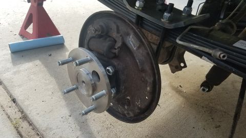 1985 Ford Bronco - A close-up view of a vehicle's rear drum brake assembly with a new wheel hub adapter installed. The vehicle is supported by a red jack stan…