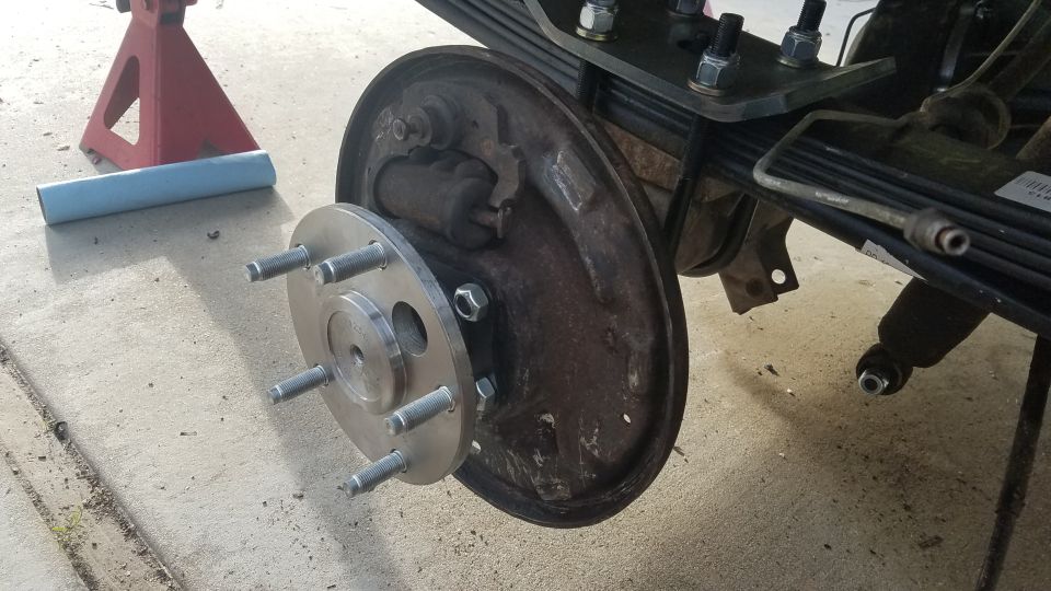 Vehicle rear drum brake with new wheel hub adapter installed, supported by jack stand.