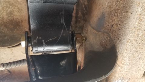 1985 Ford Bronco - A close-up view shows a black metal suspension component bolted to a rusty, textured surface, likely part of a vehicle's undercarriage. A y…