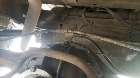 1985 Ford Bronco - The underside of a vehicle shows the rear differential and suspension components, including leaf springs and brake lines. A rusty bracket i…