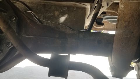 1985 Ford Bronco - A close-up view of the underside of a vehicle, focusing on the rear axle and suspension components. The image shows rusted metal parts, inc…