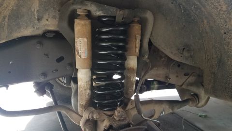 1985 Ford Bronco - The underside of a vehicle shows a suspension system with two shock absorbers and a large black coil spring. Visible labels on the shock ab…