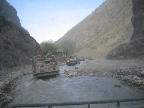 1981 Ford Bronco - Several military vehicles navigate a shallow, rocky riverbed in a , mountainous terrain.