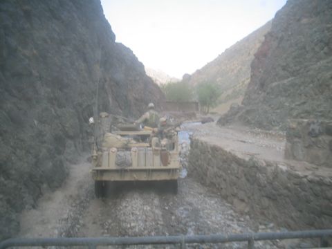 1981 Ford Bronco - A military vehicle navigates a rough, rocky path in a narrow canyon, with soldiers onboard.