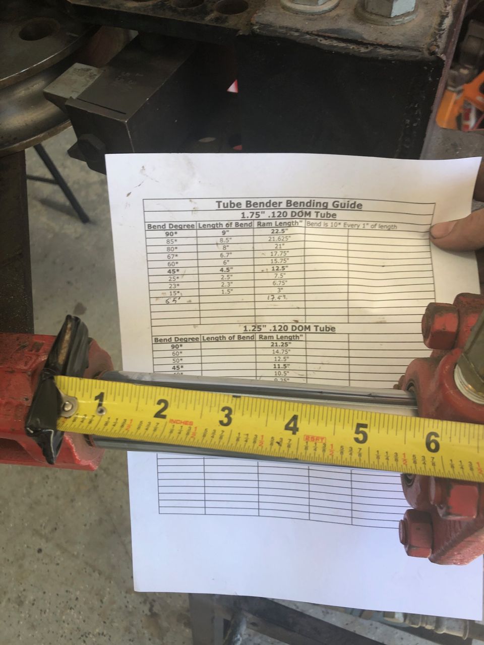 Yellow tape measure against a tube bending guide document with metal tube.