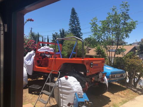 1992 Jeep Wrangler - An orange Jeep Wrangler is parked outdoors in what appears to be a driveway, with a blue vehicle partially visible behind it. The Jeep has…