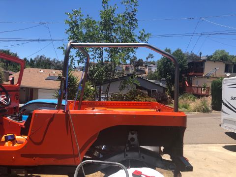 1992 Jeep Wrangler - Side view of an orange Jeep Wrangler undergoing modifications, featuring a custom roll cage and exposed frame. The vehicle is parked in a d…