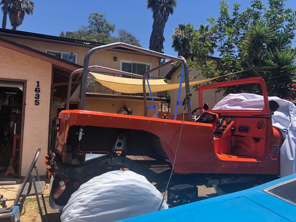 Orange Jeep Wrangler with roll cage, parked in driveway.