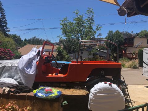 1992 Jeep Wrangler - An orange Jeep Wrangler is partially covered with a white tarp. The vehicle is outdoors in a residential driveway with houses and trees in…