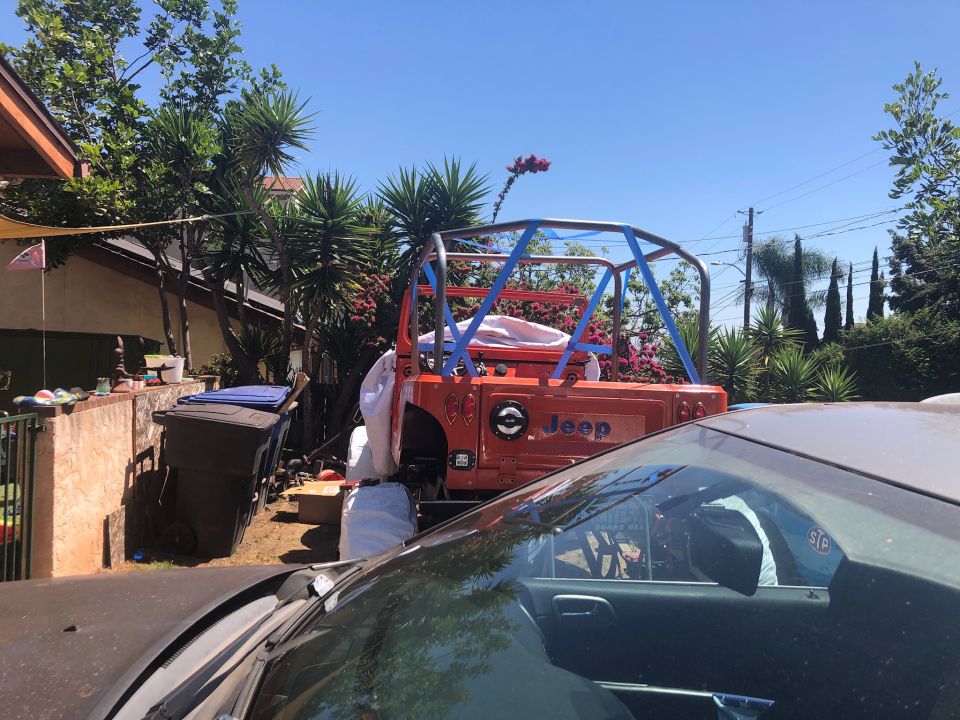 Rear view of an orange Jeep Wrangler with a blue roll cage, parked outdoors.