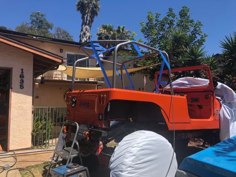 1992 Jeep Wrangler - An orange Jeep Wrangler is parked in a driveway with a custom roll cage installed. The vehicle has the word "Jeep" visible on the tailgate…