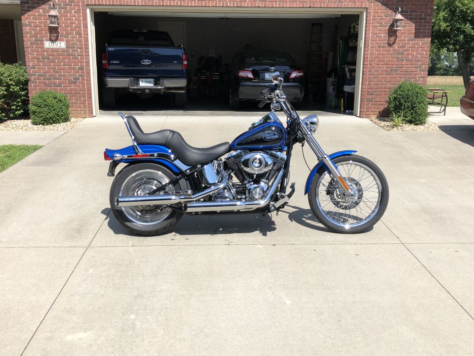 Blue and black Harley-Davidson Softail motorcycle parked in front of a garage with a Ford pickup truck inside.