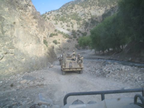1981 Ford Bronco - A military truck with soldiers drives down a rocky road next to a stream in a mountainous region.