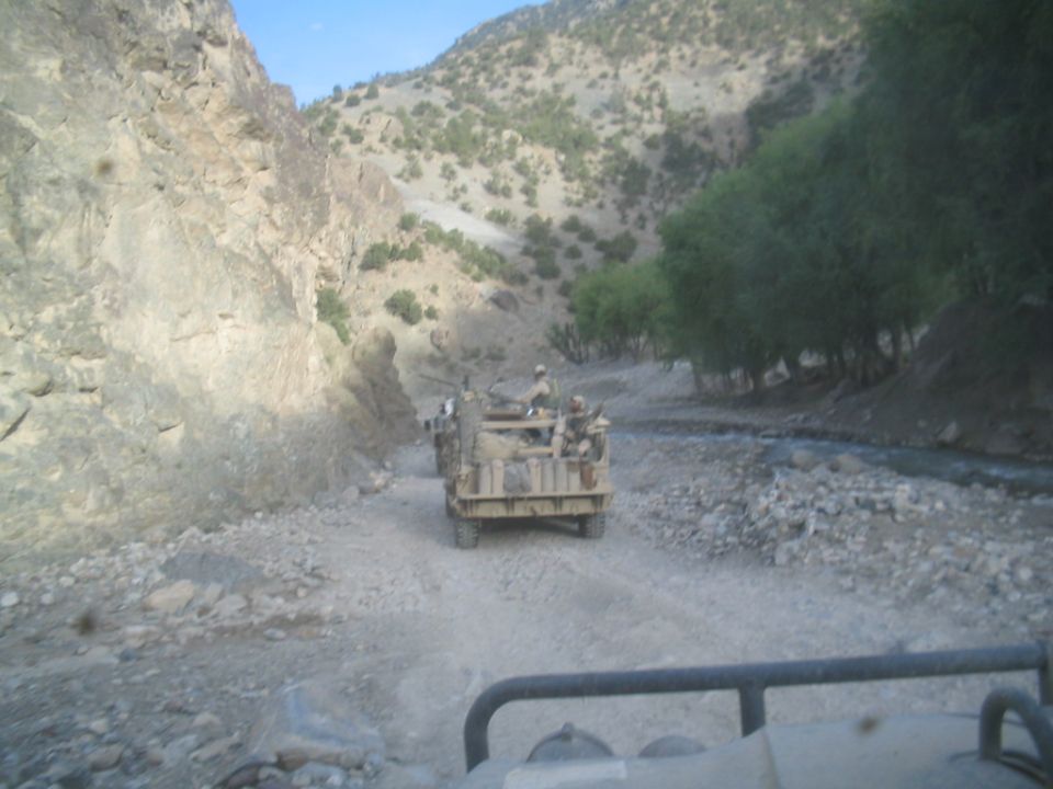 Military truck with soldiers driving on a dirt road in a mountainous area