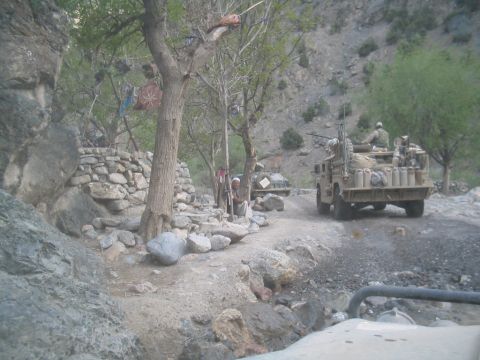 1981 Ford Bronco - Military vehicles navigate a rough dirt road through a , mountainous terrain, likely in Afghanistan.