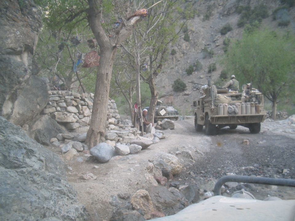 Military vehicles on a dirt road in a rocky, mountainous area